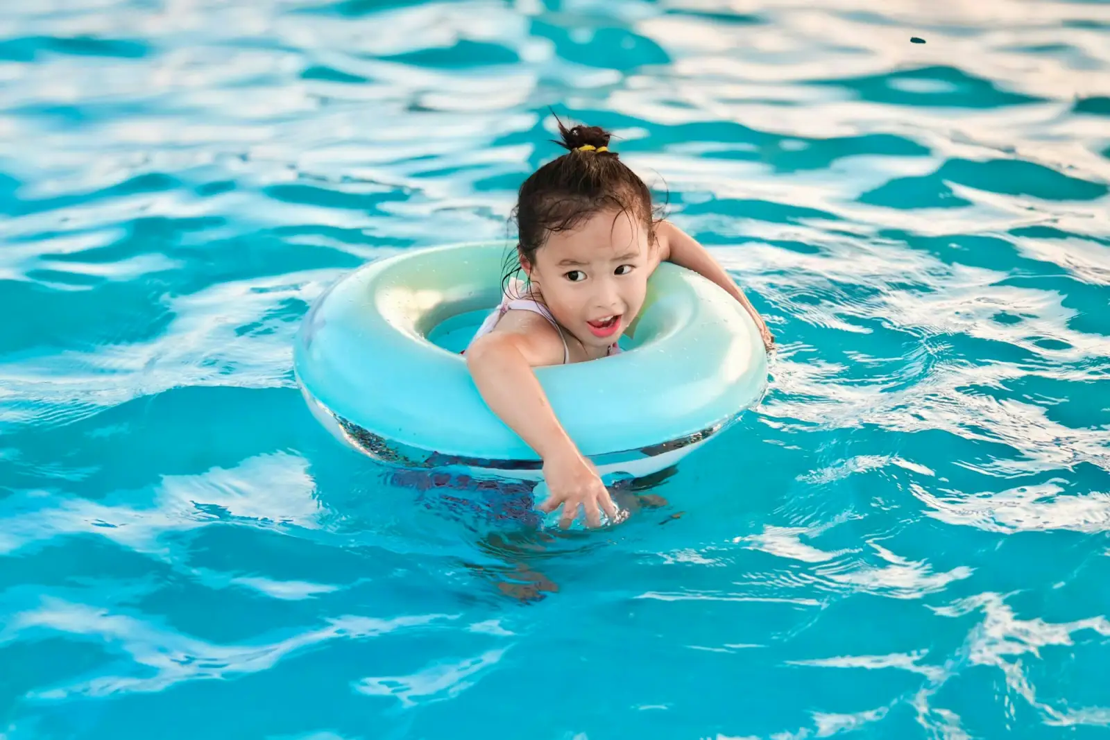 Bé gái cười tươi trong phao bơi ở hồ bơi xanh của resort gia đình Bãi Dài