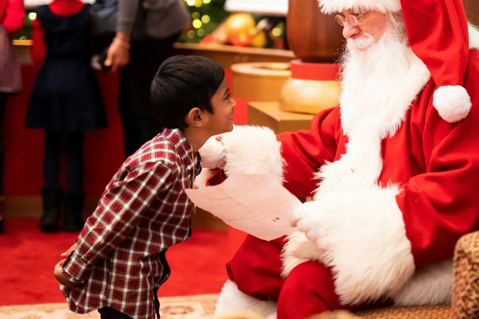 Ông già Noel trò chuyện với một bé trai bên cây thông Giáng sinh